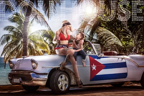 Mother and toddler on vintage white car with Cuban flag, tropical backdrop