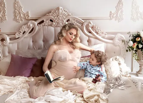 Pregnant mother in cream dress on ornate bed with toddler child