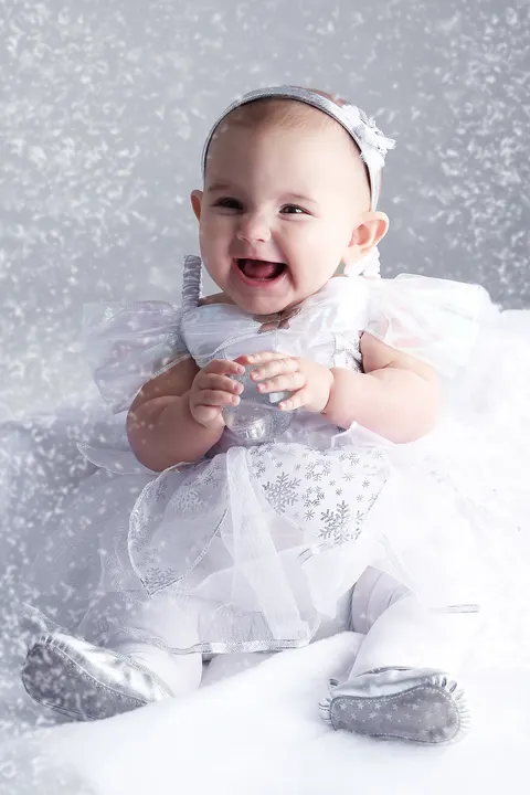 Baby girl in white tulle dress on sparkling silver background
