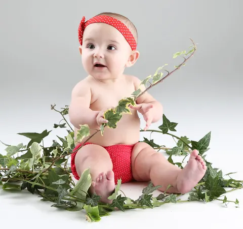 Baby in red outfit playing among ivy vines and greenery