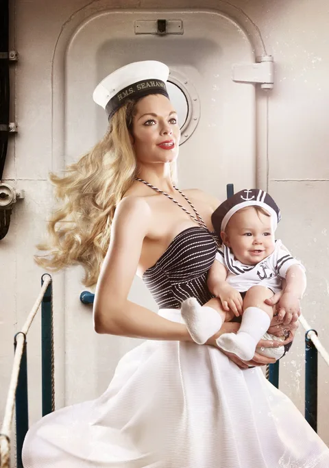 Mother in a sailor hat holding her baby in a matching sailor outfit by a ship's porthole door