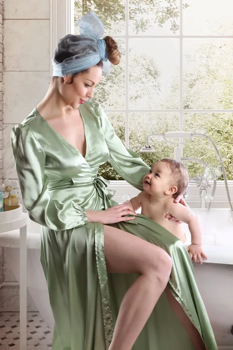 Mother in a green silk robe with her baby in a bright vintage bathroom