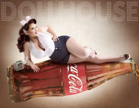 Curvy brunette pin-up in a white halter top and denim shorts lounging on a giant vintage cola bottle