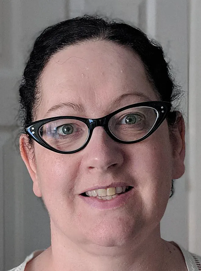 Everyday snapshot of Annabel wearing glasses in neutral grey setting, before her photoshoot transformation